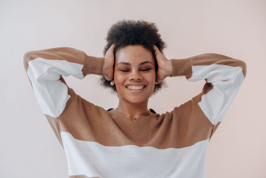 A woman wearing a brown-and-white striped top touching her head while smiling.