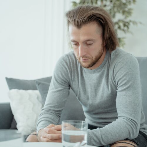 pexels-tima-miroshnichenko-5336925 A man in a gray shirt sits with his head bowed and fingers locked.