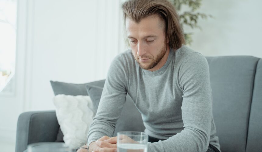 A man in a gray shirt sits with his head bowed and fingers locked.